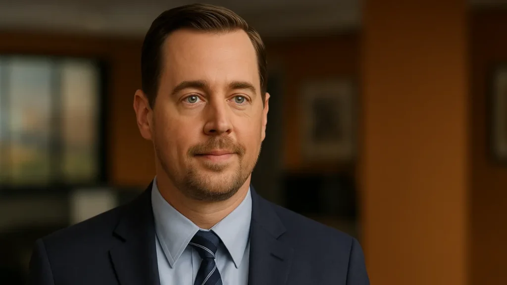 Sean Murray as Tim McGee standing in the NCIS bullpen, wearing a suit and tie under natural office light.