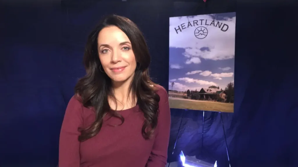 Heartland star Michelle Morgan smiling beside a Heartland poster during an interview