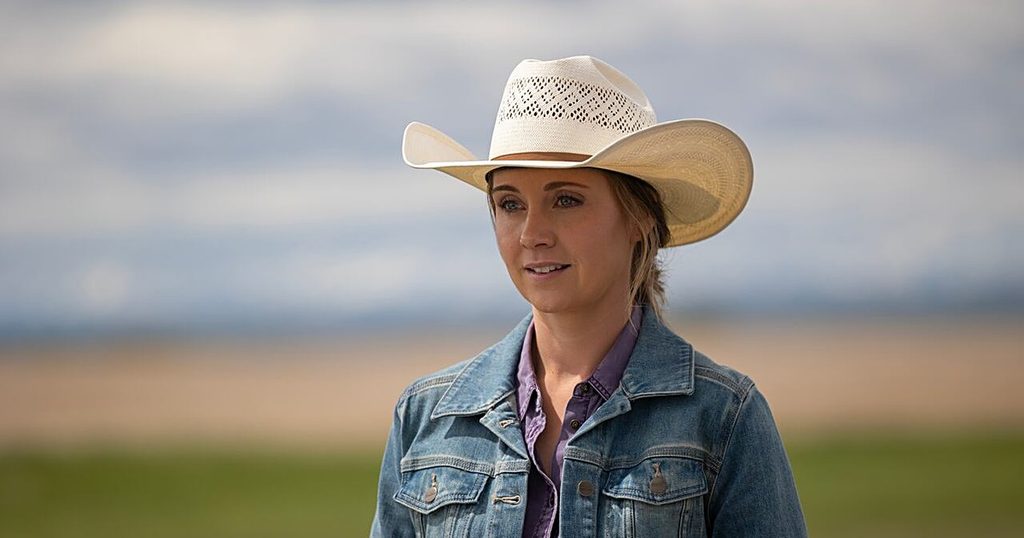 Amy Fleming (Amber Marshall) in a cream cowboy hat and denim jacket, looking off to the side on the Alberta prairie in Heartland