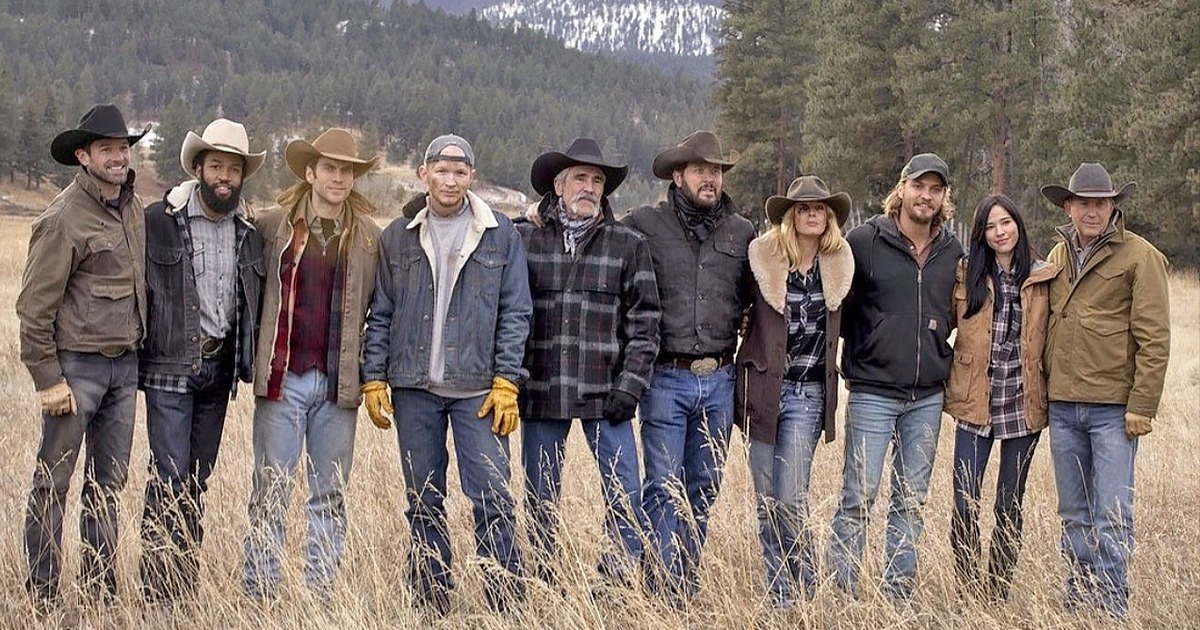 Yellowstone cast standing together on the Dutton ranch with Montana mountains behind them, including Kevin Costner as John Dutton