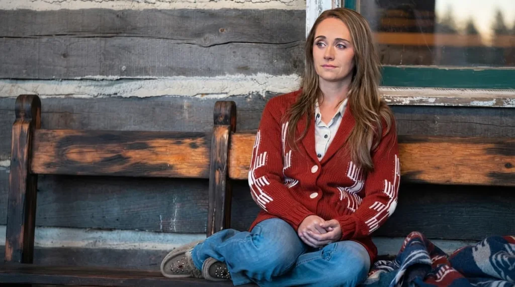 Amber Marshall as Amy Fleming with a poignant, tearful expression on the rustic wooden bench of the Heartland ranch cabin.